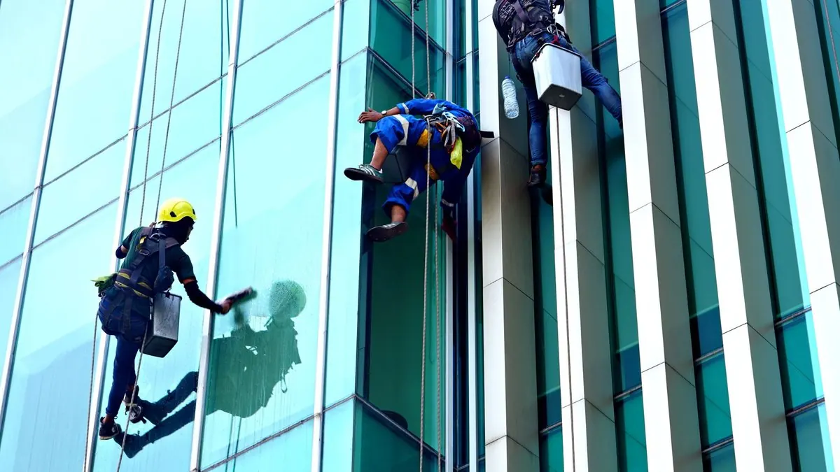Trois laveurs de vitres sur cordes nettoient la façade vitrée d’un immeuble moderne